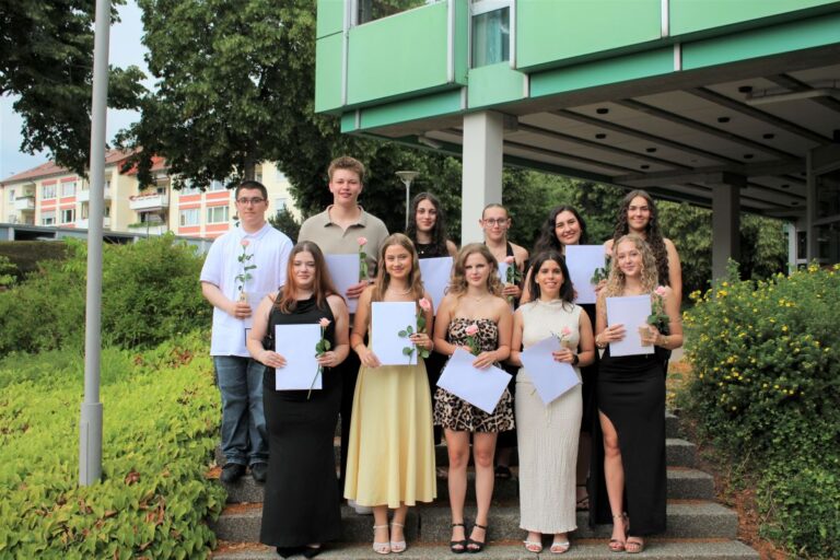 Die Preisträgerinnen und Preisträger der Berufsfachschule stehen mit ihren Zeugnissen auf einer Treppe vor dem Schulhaus