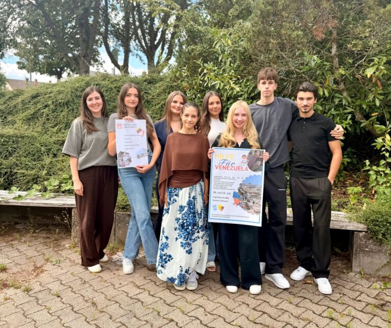 Schülerinnen und Schüler der SMV mit ihrer Lehrkraft stehen zusammen und halten das Plakat in die Kamera, welches zur Spende für Venezuela aufruft.